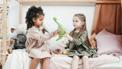 siblings playing a green plush toys